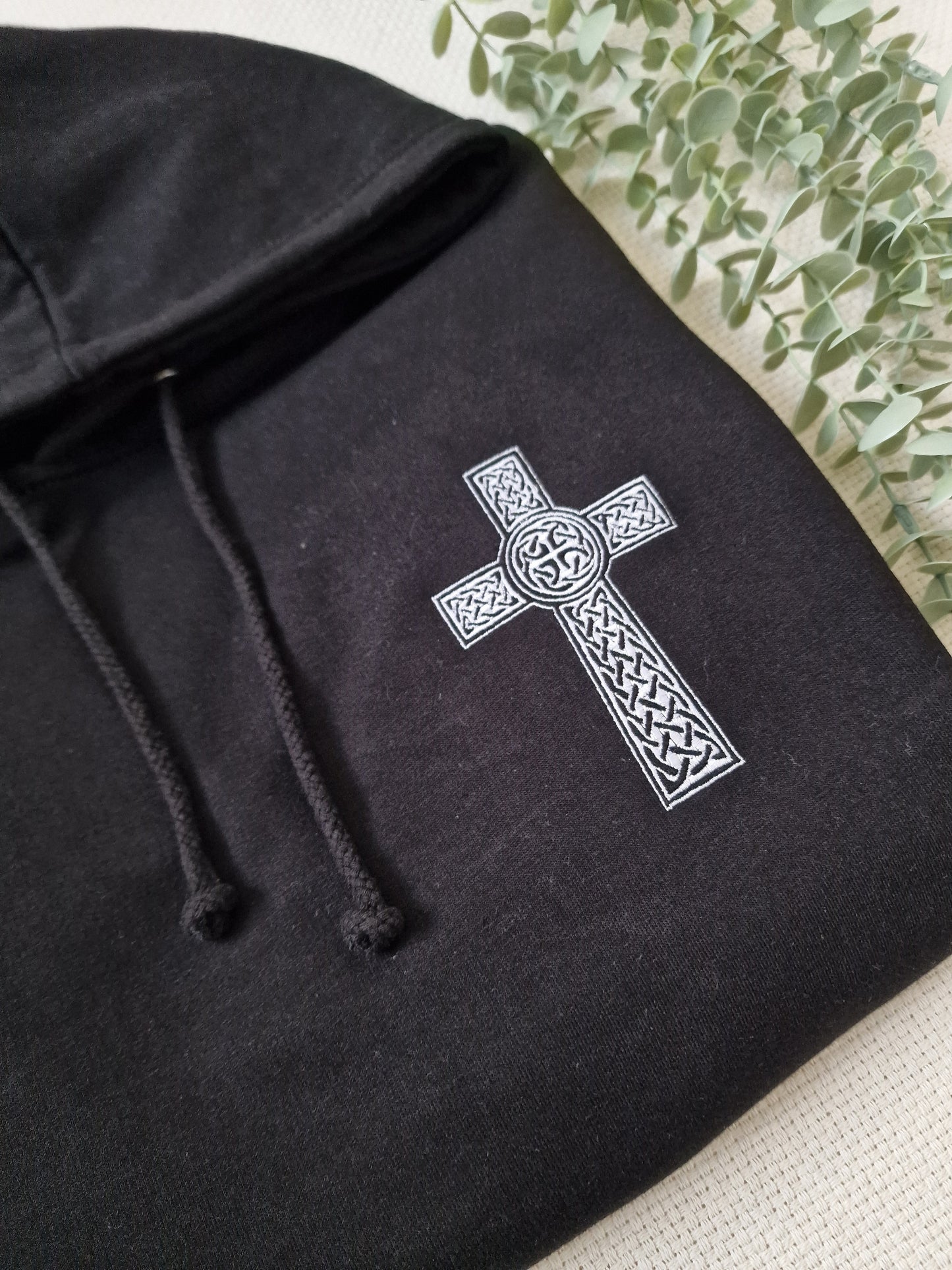 Black hoodie with white embroidered Celtic cross and intricate patterns on the front.