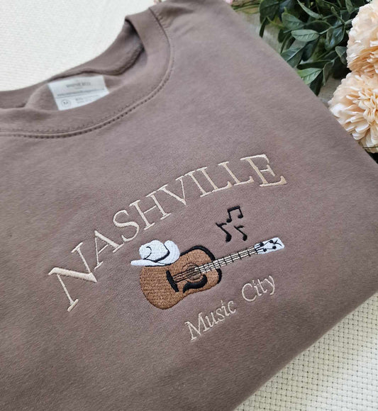 A brown fleece sweatshirt with 'Nashville' text and a musical guitar graphic on the front.