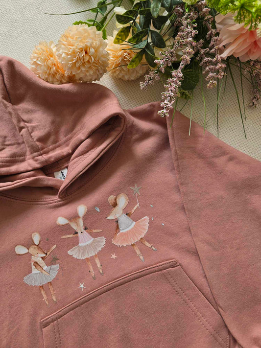A pink sweatshirt with an embroidered design of ballet dancers and mice, presented alongside flowers.