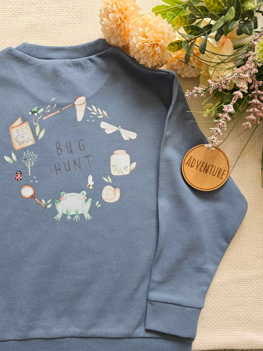 A blue sweatshirt with a graphic design of various elements and the text 'BUG HUNT' on the back, presented next to some bug icons.