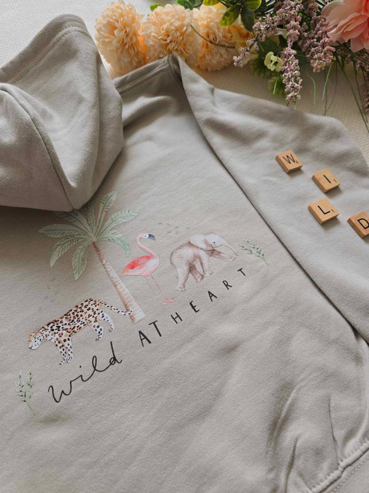 A beige kids sweatshirt/hoodie with an animal and nature themed design, including a flamingo and palm trees, and the text 'WILD AT HEART'.