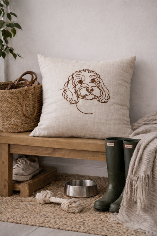 Personalised embroidered dog line art cushion on a wooden bench in a cosy home setting