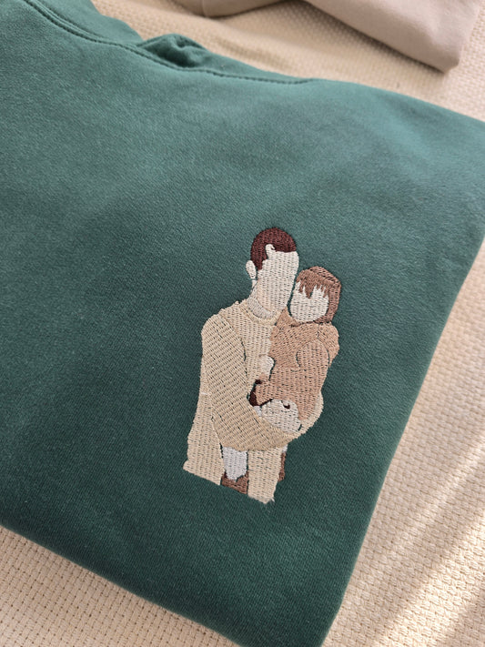 A green sweatshirt with a personalized embroidered design of a family embracing.